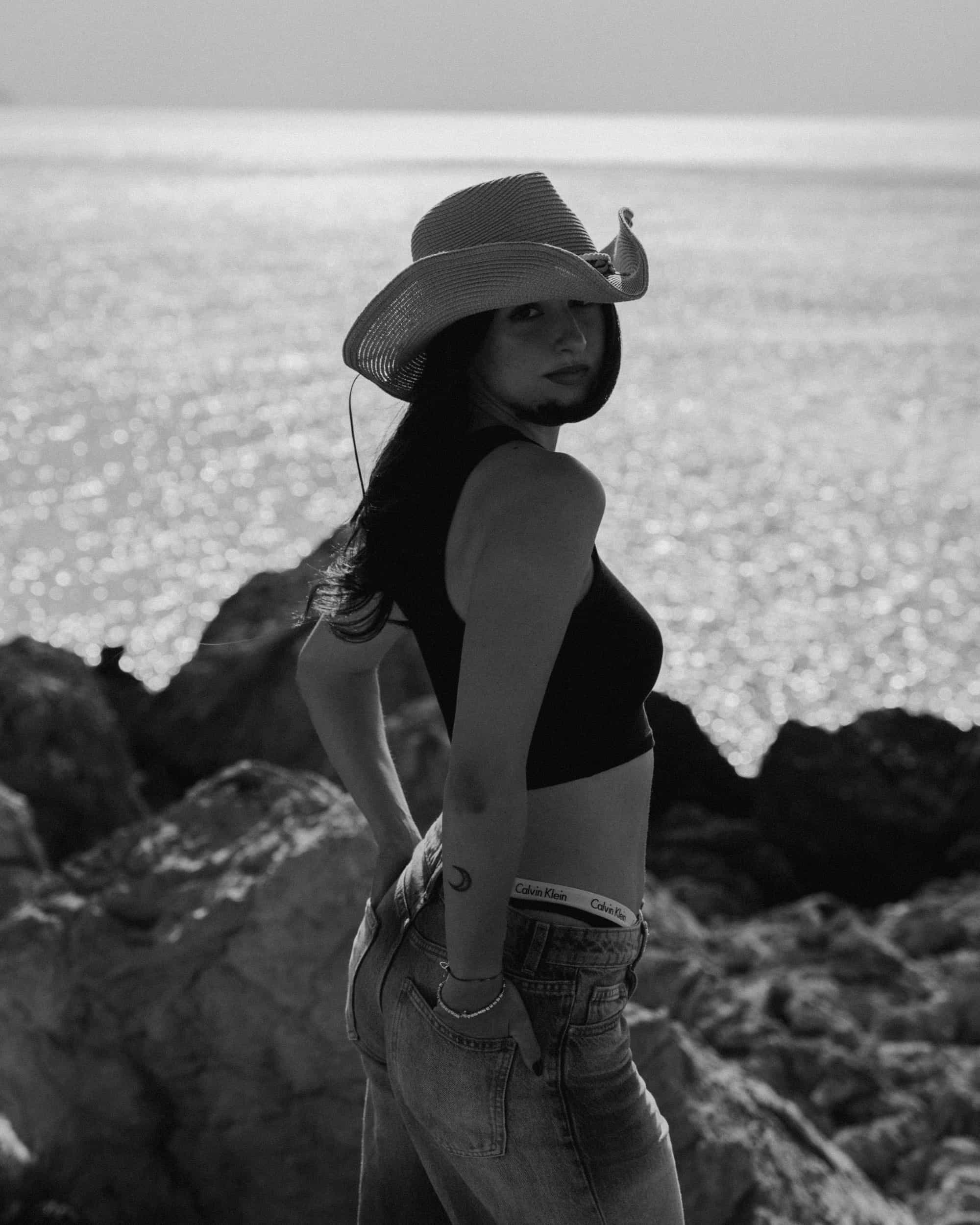Portrait of a woman in a cowboy hat standing on coastal rocks, editorial photography