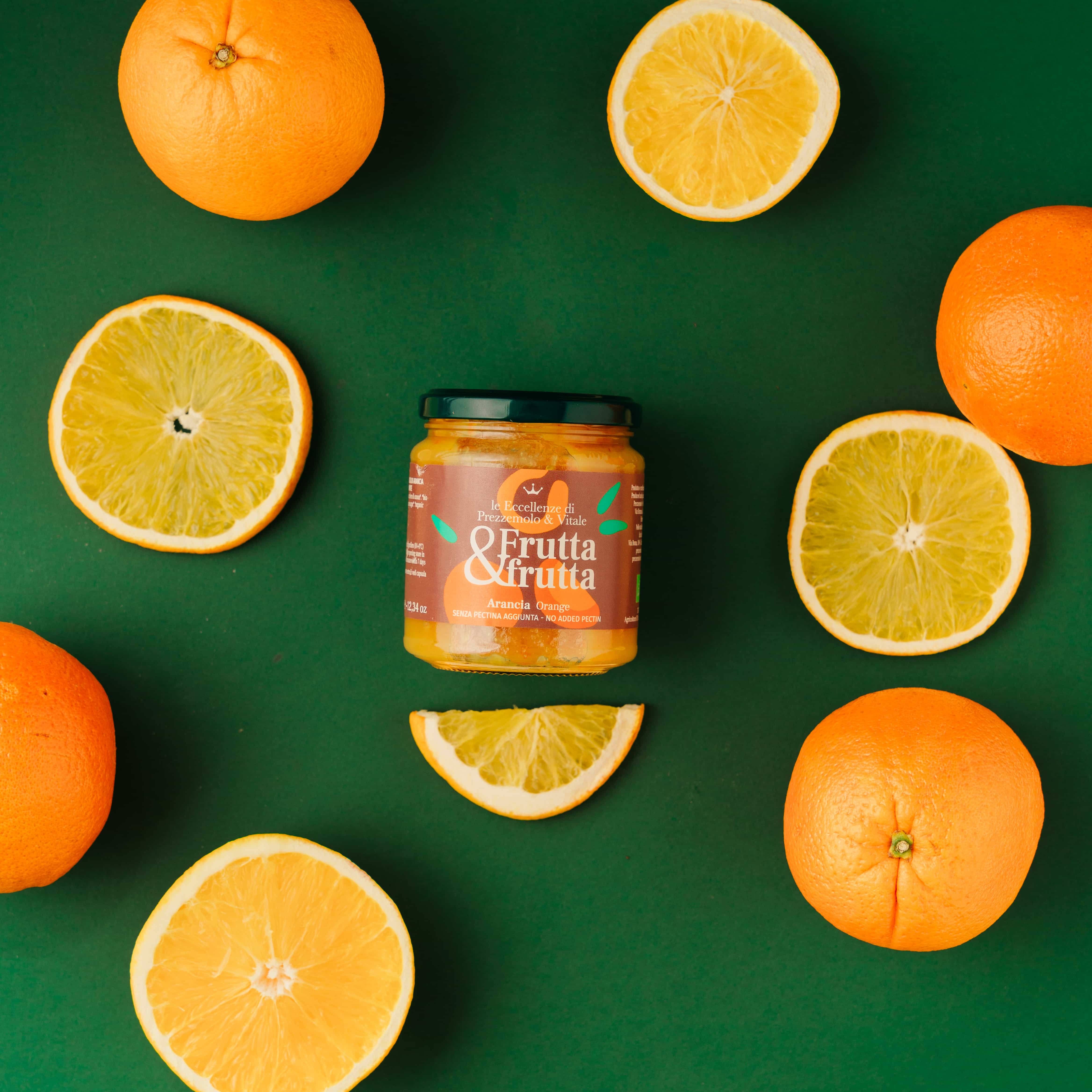 A top down photo of an orange jam with some oranges on the tabletop