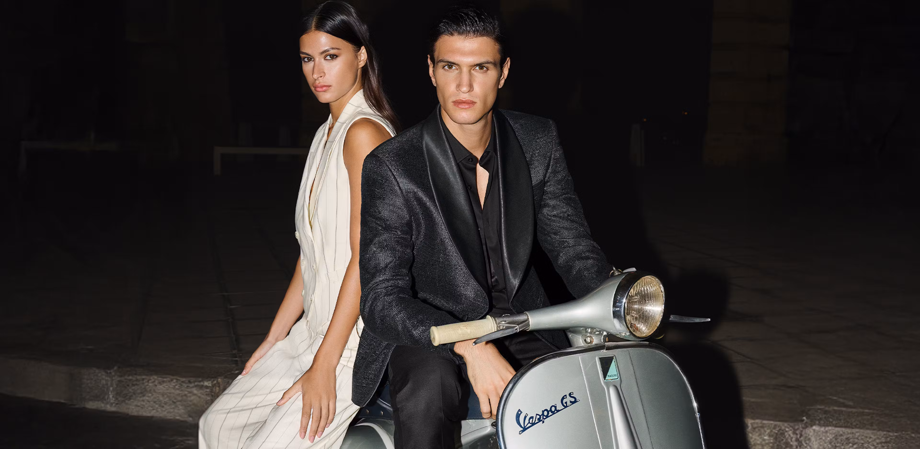 joop lady and gentleman sitting on vespa, she with white striped trouser suit and he with black dinner jacket