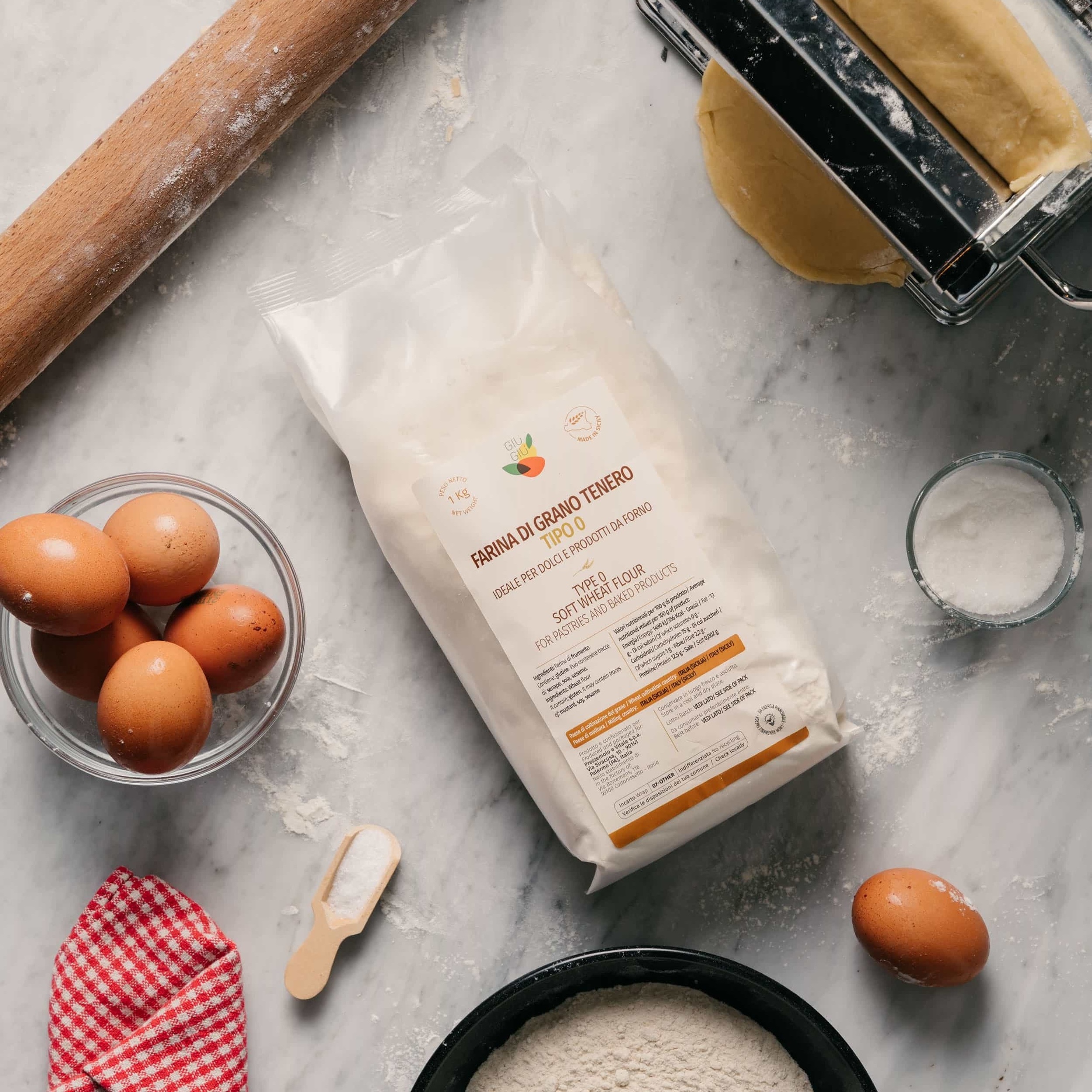 Package of Sicilian black bread flour on a marble surface with bread rolls, some eggs, rolling pin