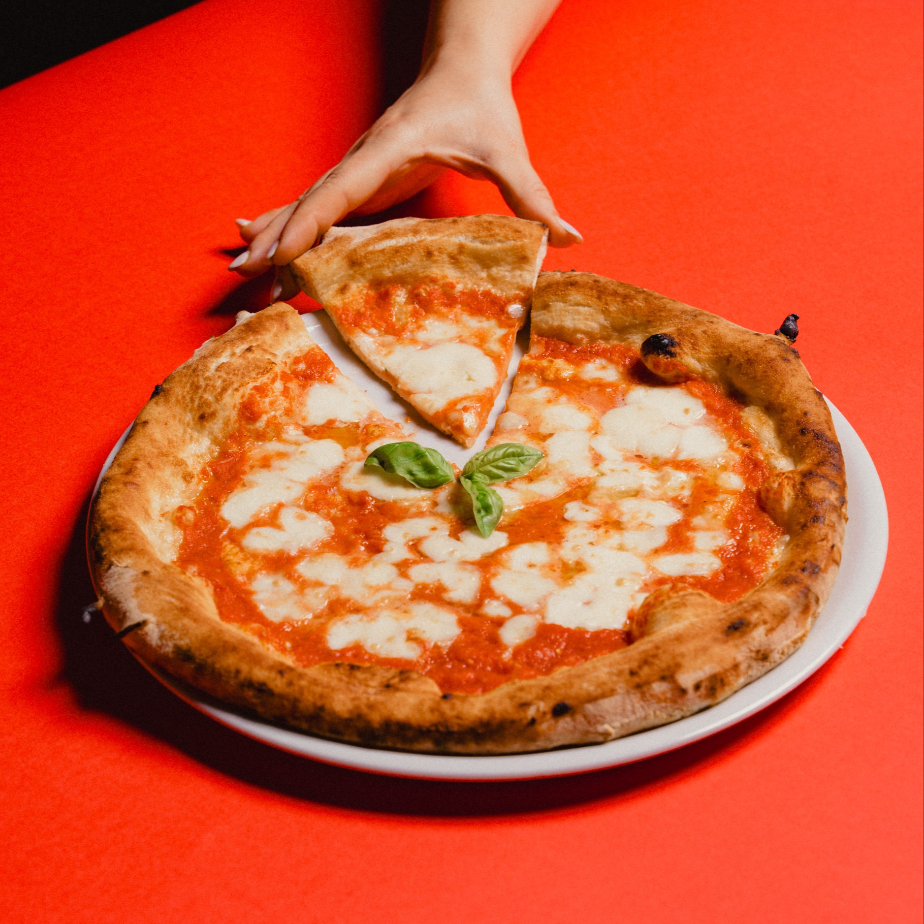 A photo of a margherita pizza with a hand picking up a quarter